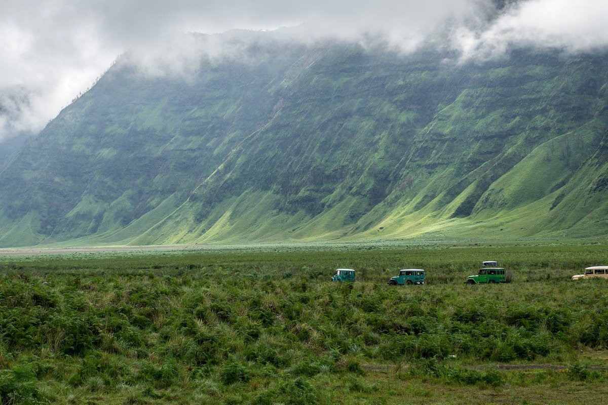 Hamparan savana kering dengan beberapa jeep wisata dan bukit berjajar di kawasan Bromo.